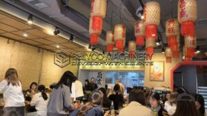 This is a lively grilled fish restaurant where our team is gathering for a group lunch. Traditional paper lanterns with red tassels hang from the ceiling. It has a warm, bustling atmosphere."